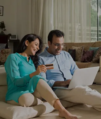 A couple sitting on a couch using a laptop while reviewing a card and marketing an online payment | ICICI bank.