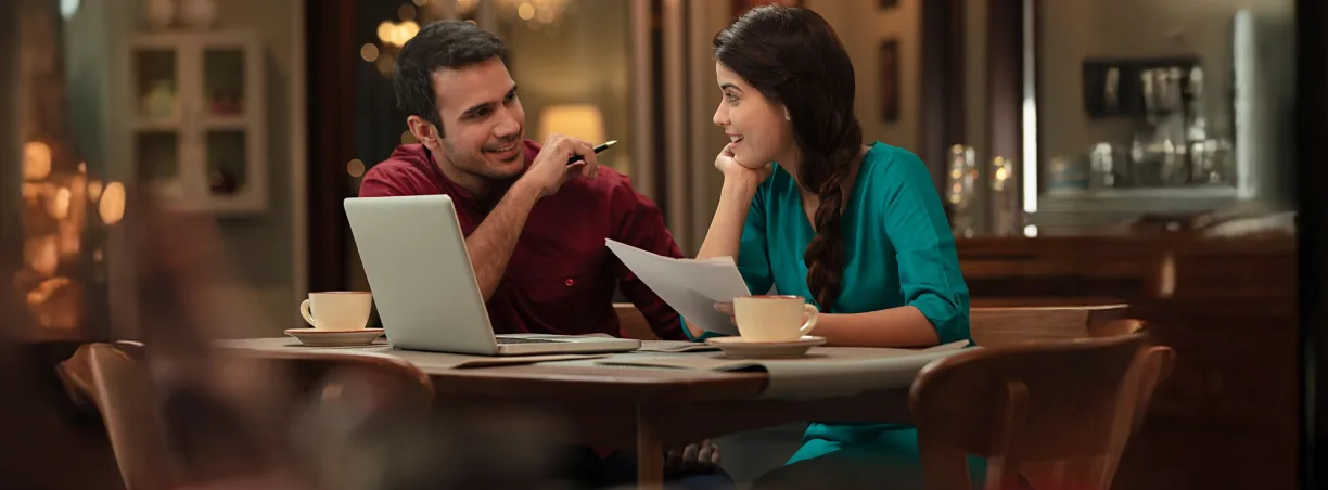 Two people sitting at a table with a laptop and documnets on a webpage banner from ICICI Bank.