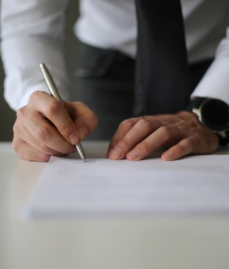 Close-up a person writing on a blank sheet of paper with both hands visible on a desk | ICICI Bank.